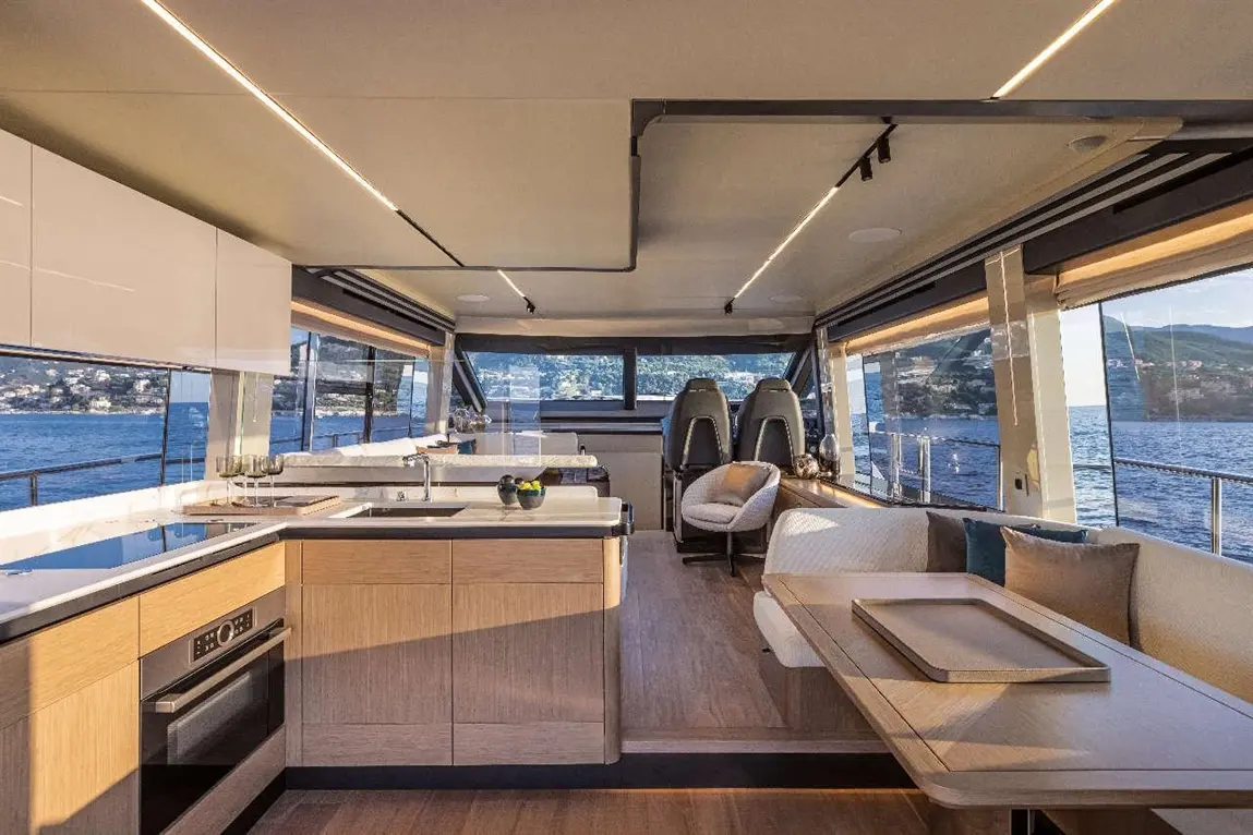 Modern yacht interior featuring a spacious kitchen, dining area, and large windows overlooking the water and landscape.